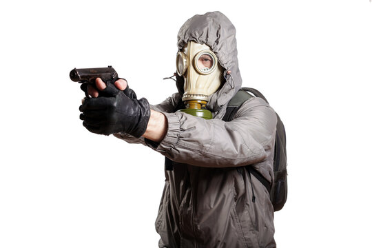 An isolated shot of a man dressed in a gas mask, a hooded jacket, a backpack, gloves, holding a gun in his hands and aiming to the left. On a white isolated background