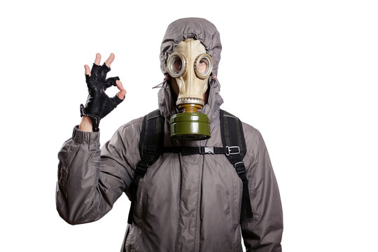 An isolated shot of a man dressed in a gas mask, a hooded jacket, a backpack, shows a gesture of ok, looks into the camera. On a white isolated background
