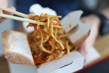 Man eating chinese noodles with chopsticks out of paper box closeup