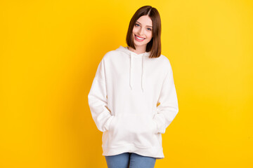 Photo of pretty lovely cheerful lady hands pockets posing wear white sweatshirt isolated yellow...