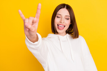 Portrait of attractive dreamy cheerful girl showing horn sign having fun grimacing isolated over bright yellow color background