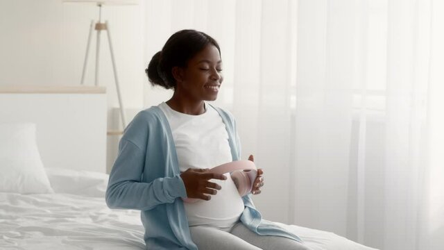 Happy Black Pregnant Lady Holding Headphones Near Belly, Playing Music To Baby