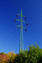 Obraz premium High voltage eletrical towers and lines with beautiful blue sky above colorful autumn trees. Eletricity towers. High-voltage transmission lines. Electricity transmission towers.