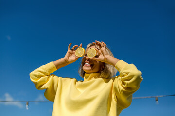 Cheerful woman holding slice of lemon in front of eyes during sunny day