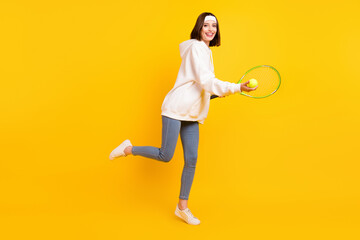 Fototapeta na wymiar Photo of cheerful sportswoman hold racket ball wear headband hoodie jeans shoes isolated yellow color background