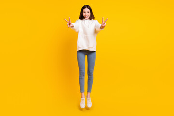 Fototapeta na wymiar Full length body size view of pretty cheerful girl jumping showing v-sign having fun isolated over bright yellow color background
