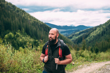 Man hiking in mountains with heavy backpack travel wandering lifestyle adventure concept summer vacation outdoors alone in the wild. Handsome bald bearded young man.