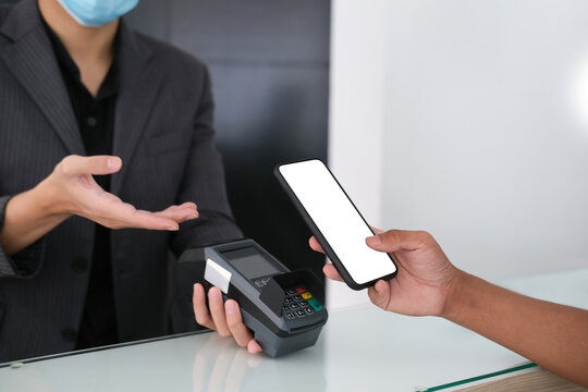 Cropped image of customer's hand holding a white blank screen smartphone for doing a payment. Concept of using a digital payment and less down touching things for prevention of a virus infection.