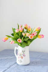 Beautiful spring bouquet of pink tulips in a jug on the table, flowers in a home interior