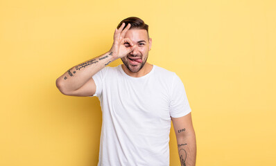 young handsome man smiling happily with funny face, joking and looking through peephole, spying on...