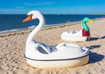 Closeup shot of swan pedal boats on the sand of the beach with the blue sea in the background © Mirco Vacca/Wirestock