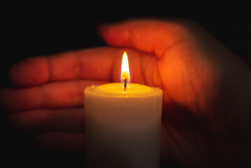 One palm take care of candle fire at night.Selective focus,Dark black background.Closeup.