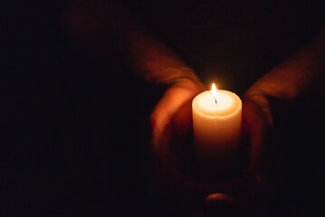 Hands holding burning candle in dark like a heart.Selective focus,black background.Copy space.