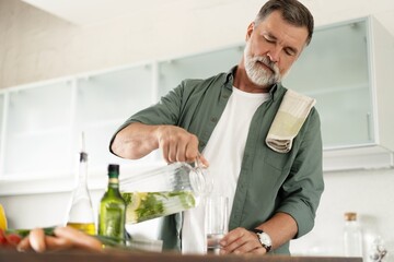 Fototapeta Smiling mature man with recipe book pours fresh lemonade in kitchen. obraz