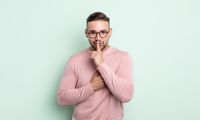 young handsome man looking serious and cross with finger pressed to lips demanding silence or...