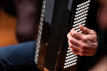 An accordion players hand placed on the buttons of a black accordion