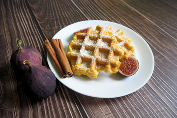 on a white round plate with pieces of figs and cinnamon sticks on a wooden table are two Belgian cornmeal waffles, eggs and pumpkin. side view. gluten-free and lactose-free homemade food