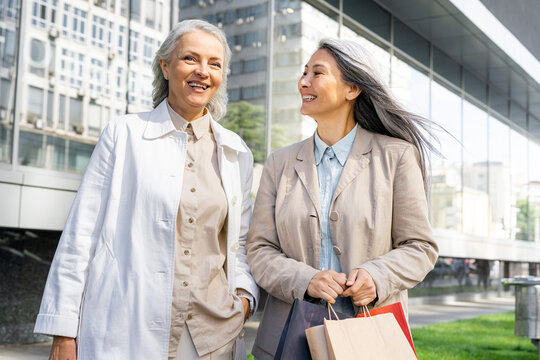 Woman with shopping bags talking with female friend in front of mall