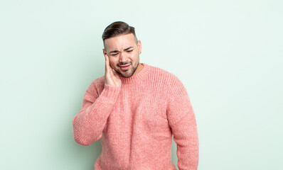 young handsome man holding cheek and suffering painful toothache, feeling ill, miserable and...