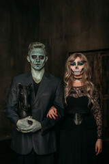 The image of a skeleton girl and the image of a Frankenstein man on Halloween in the dark. an image for a couple on Halloween. a woman and a man stand straight. A man holds a black horse in his hands