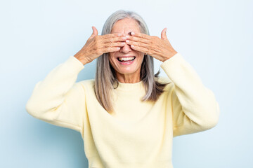 middle age gray hair woman smiling and feeling happy, covering eyes with both hands and waiting for...