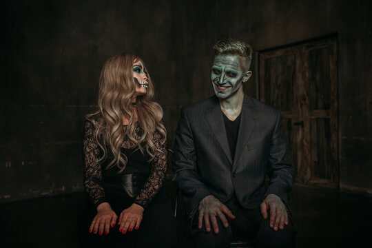 The image of a skeleton girl and the image of a Frankenstein man on Halloween in the dark. an image for a couple on Halloween. both are sitting and laughing