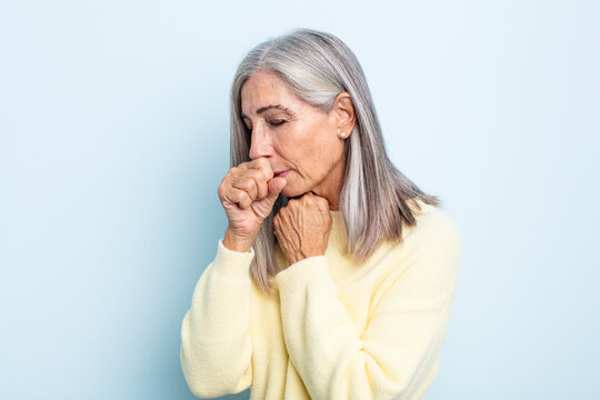 middle age gray hair woman feeling ill with a sore throat and flu symptoms, coughing with mouth covered