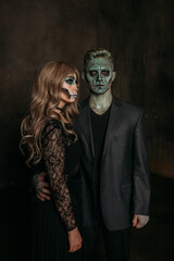 The image of a skeleton girl and the image of a Frankenstein man on Halloween in the dark. an image for a couple on Halloween. a woman in front, a man behind and looking at the camera
