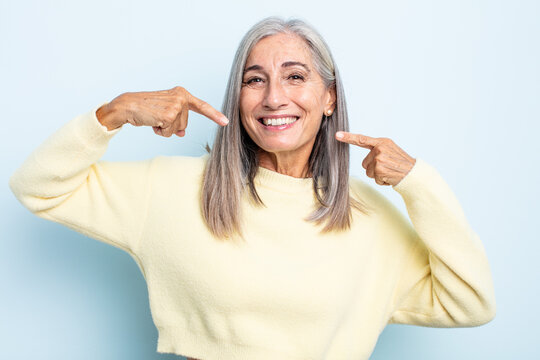 middle age gray hair woman smiling confidently pointing to own broad smile, positive, relaxed, satisfied attitude