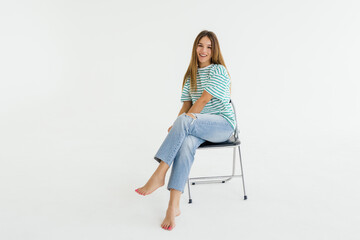 Beautiful young woman sitting on a chair and smiling, isolated over white background