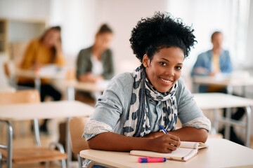 Happy African American woman writes exam while attending class at the university and looking at...