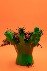 Green hand holding yew branches with red berries and two spiders. Halloween decoration concept