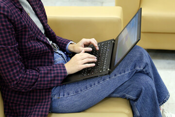 Girl in jeans and checkered jacket sitting on leather sofa with laptop on her knees. Dress code, businesswoman, work in office