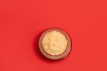 Face cream in glass cosmetic jar on a color background