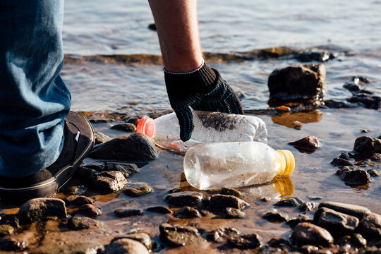 Male activist collecting plastic bottles at riverbank