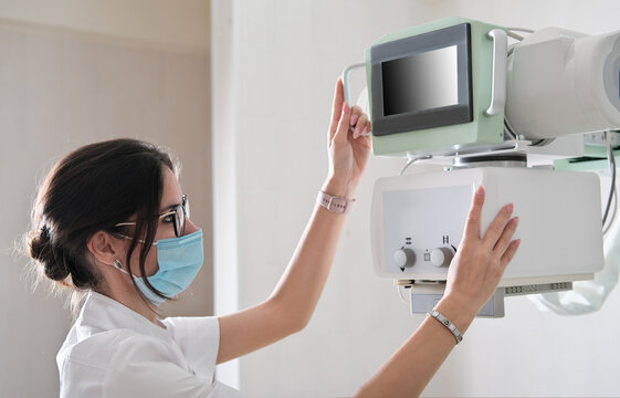 Hospital Radiology Room: Beautiful Multiethnic Woman adjusting X-Ray Machine in Modern Clinic Office. technician in radiology department turning on scanner. to take animage