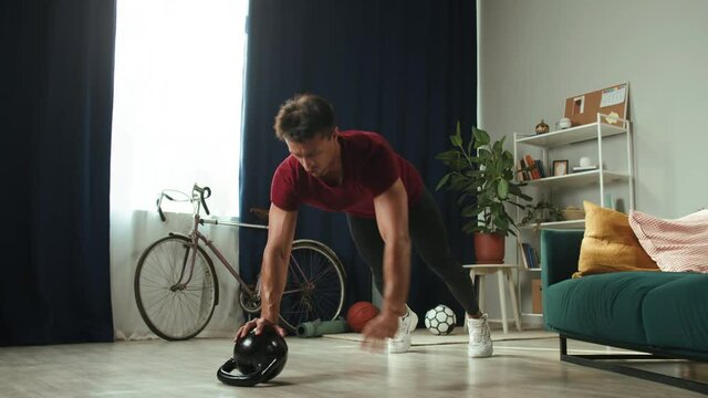 Sportsman doing push-ups standing on kettlebell. Professional trainer, strong athlete champion exercising on floor in living room. Home gym concept, remote workouts during coronavirus isolation.
