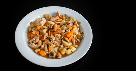 A traditional Chinese dish of chicken stew, with almonds, carrots and pasta. In a plate on a black background, close-up.