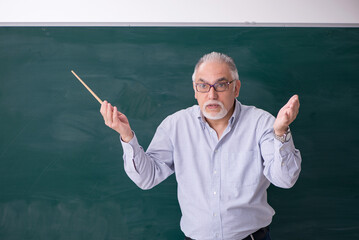 Old male teacher in front of green board