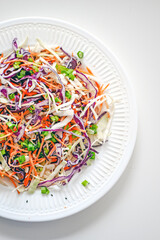 Coleslaw cabbage salad with cabbage, carrots, herbs and sesame seeds on a white plate. Healthy eating, vegan food.