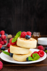 Cottage cheese pancakes with fresh berries, sour cream and honey on a dark wooden background. Homemade traditional Ukrainian and Russian syrniki.