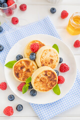 Cottage cheese pancakes with fresh berries, sour cream and honey on a white wooden background. Homemade traditional Ukrainian and Russian syrniki.