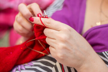 Woman knits with knitting needles red sweater from natural woolen threads