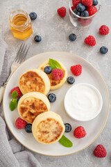 Cottage cheese pancakes with fresh berries, sour cream and honey on a gray concrete background. Homemade traditional Ukrainian and Russian syrniki.