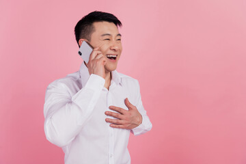 Profile side photo of young asian guy laughter joke speak cellphone call online isolated over pink color background