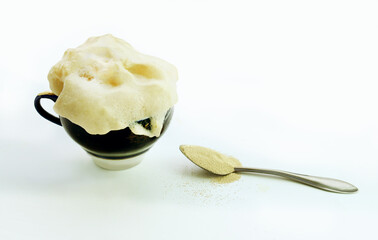 Close-up of sponge dough in a cup next to a spoon with dry yeast. Preparation for yeast dough.