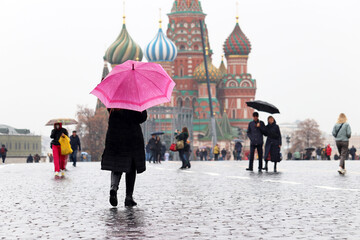 Rain in Moscow, woman with pink umbrella walks on people background on Red square against the St...