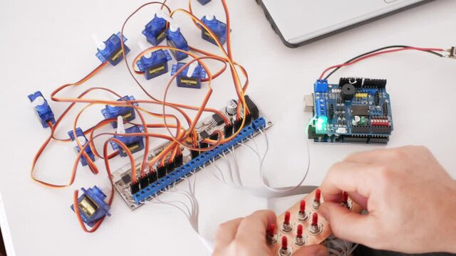 A male programmer creates robotics, an arduino board controls servo motors. DIY mechanics, programming through codes on a laptop. Technologies of the future. controls