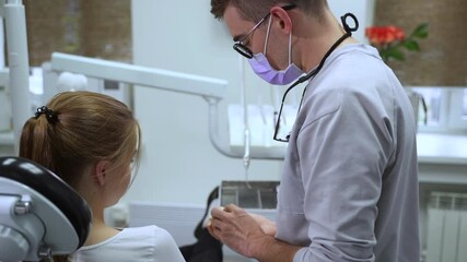 Orthodontist consults client. Dentist practitioner in grey uniform shows teeth problem on cast teeth model spbas to patient at appointment in hospital office