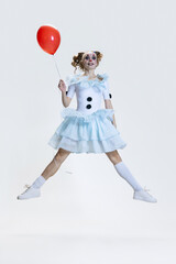 Full-length portrait of young girl wearing Halloween dress, costume of clown jumping isolated over grey background